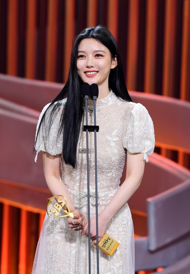 คิมยูจองในชุดเดรสลูกไม้สีขาวสง่างามพร้อมถ้วยรางวัลเกียรติยศ
